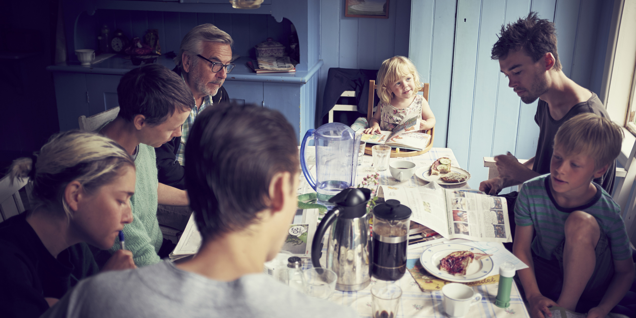 Familj i olika åldrar som äter frukost mot blå vägg
