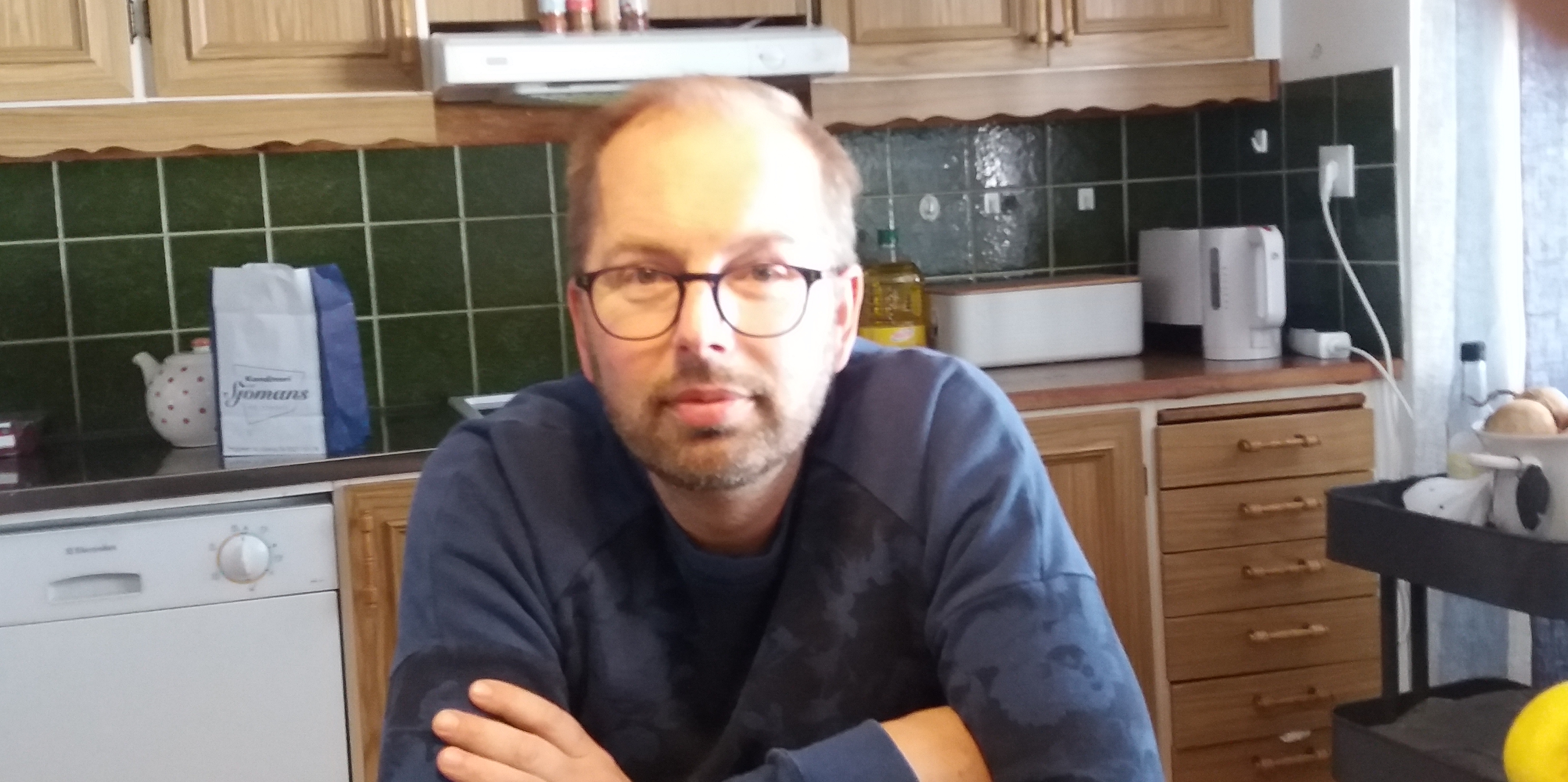 Joachim sitter i sitt kök och ler in i kameran