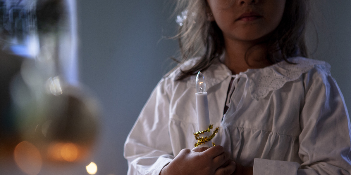 En person klädd till lucia står med ett ljus i handen