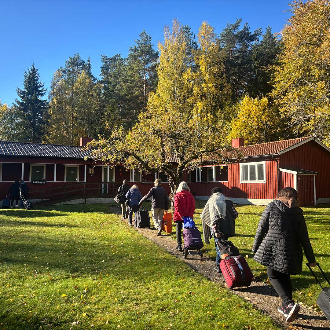 Deltagare på Stockholms Stadsmissions seniorkollo går på rad mot ett hus med sina resväskor.