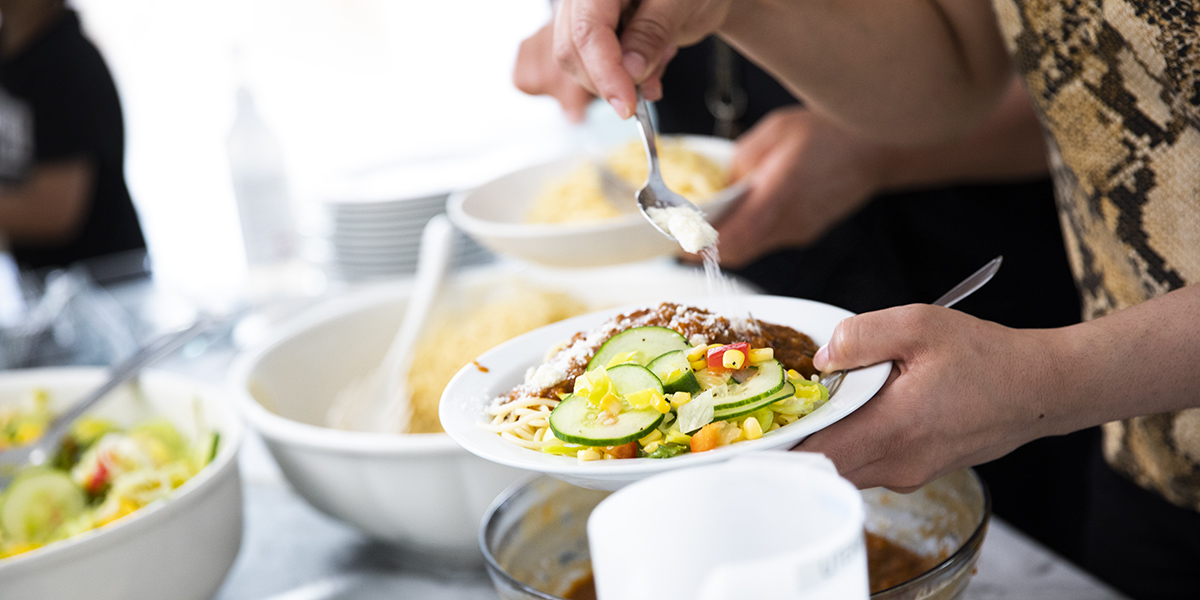 En hand strör över parmesan på en portion mat.