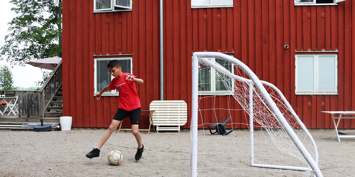 Pojke leker med sin fotboll på en grusplan 