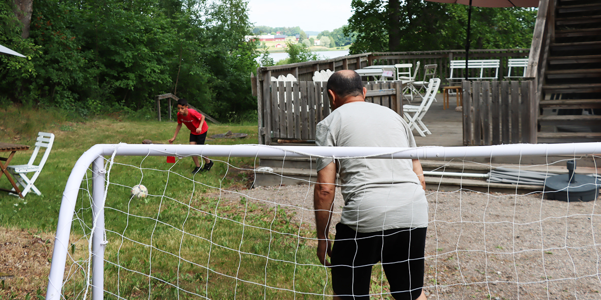 Pojke spelar fotboll med en man på kollo.