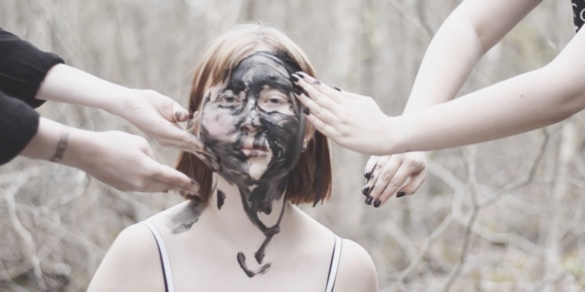 Flicka som får lera insmetad i ansiktet av fyra händer