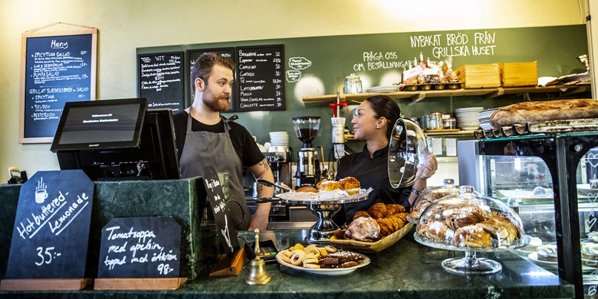 Personal på Café Eugenia pratar med varandra bakom disk med gott fikabröd.