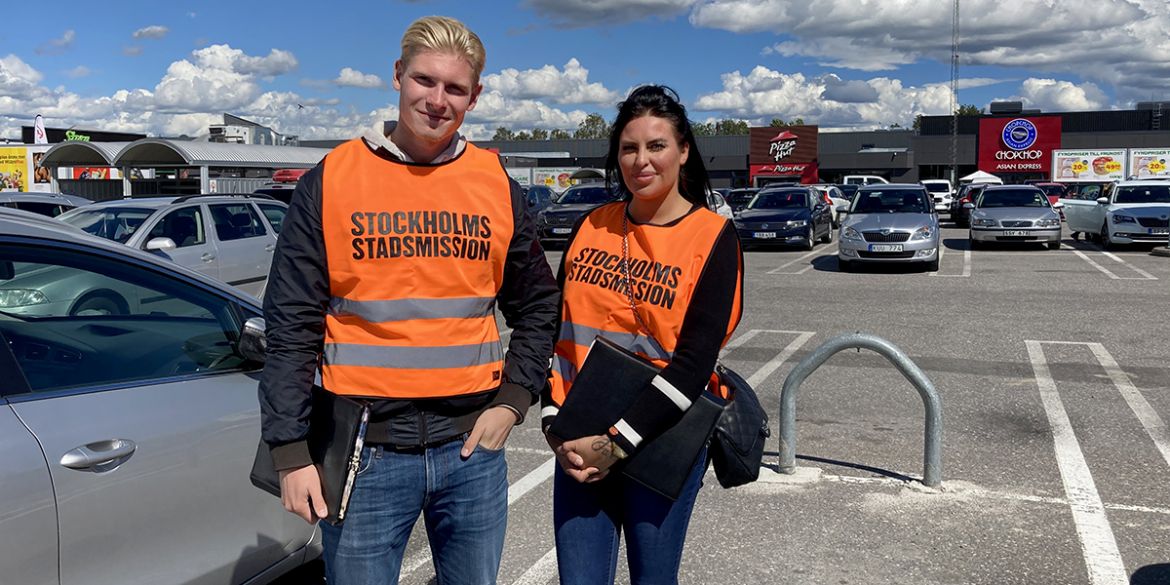 Två värvare från Stockholms Stadsmission på en parkeringsplats vid ett köpcentrum.
