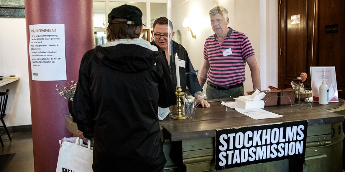 En mansperson ger en matlåda till en en annan man. Ytterligare en man står bredvid och tittar.