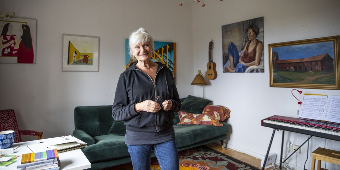 Kvinna står mitt i ett rum framför en soffa som har tavlor på väggarna. Kvinnan heter Lily och är hyresvärd för Stockholms Stadsmission.