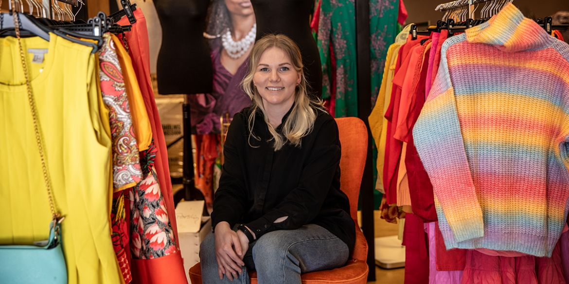 Foto: Anna Z Ek Butikschef sitter i en fåtölj med kläder omkring sig.
