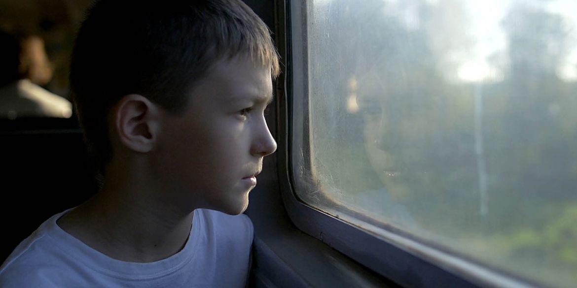Pojke sitter på tåg och tittar ut genom fönstret på tåget.