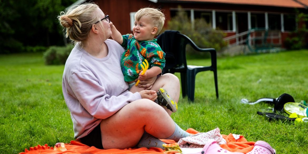 Mamma och barn sitter på gräset på en filt.