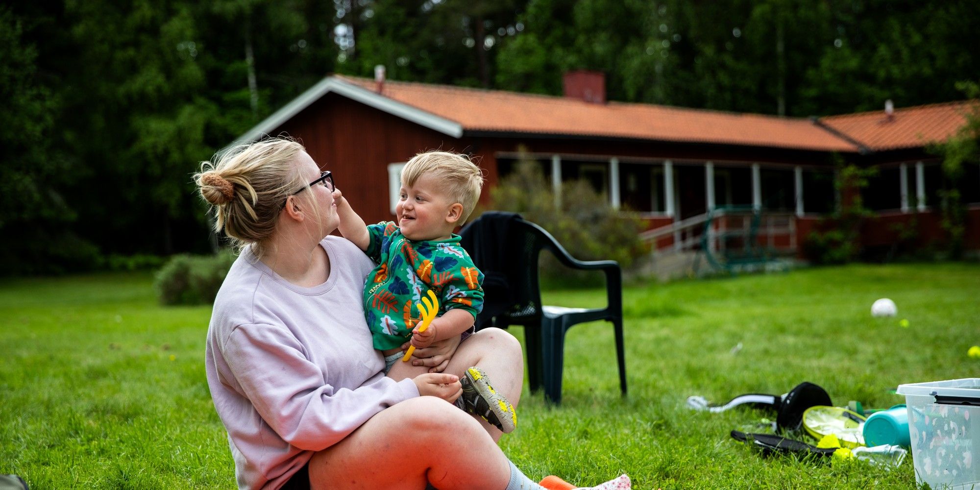 En kvinna sitter på en gräsmatta med ett barn i famnen.