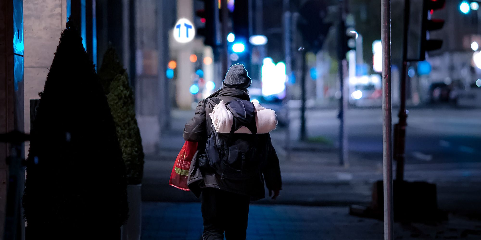 Kvinna med ryggsäck går på en gata mitt i natten. Kvinna går på en gatan mitt i natten med sina tillhörigheter i en ryggsäck på ryggen.