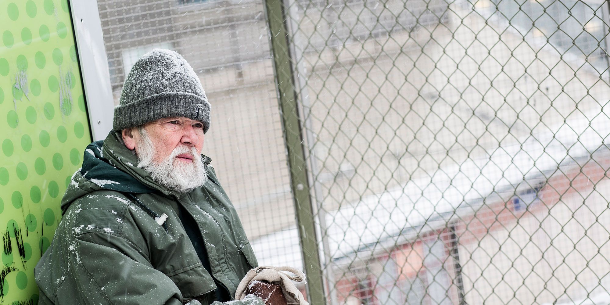 Frusen man utomhus med snö på mössa och jacka
