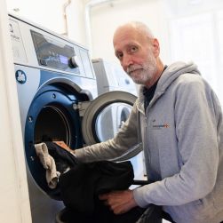 En man stoppar in tvätt i en tvättmaskin på vår dagverksamhet för män i hemlöshet.