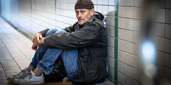 En man i hemlöshet sitter mot väggen i en tunnel.