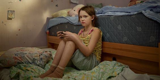 Flicka sitter på golvet och lutar sig mot sängen i ett sovrum.