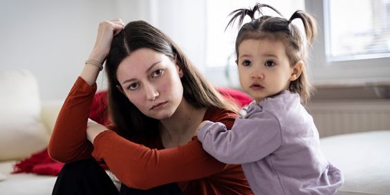 En mamma och hennes dotter sitter i ett vardagsrum och tittar in i kameran.