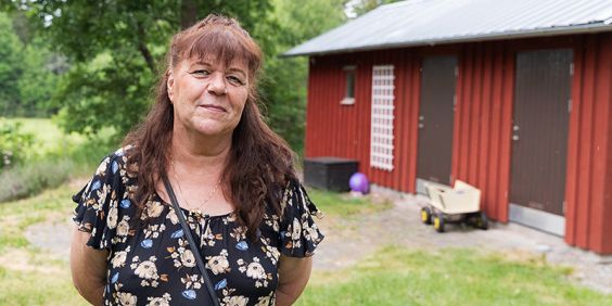 Kolloledare står utomhus och tittar in i  kameran med rött hus i bakgrunden.