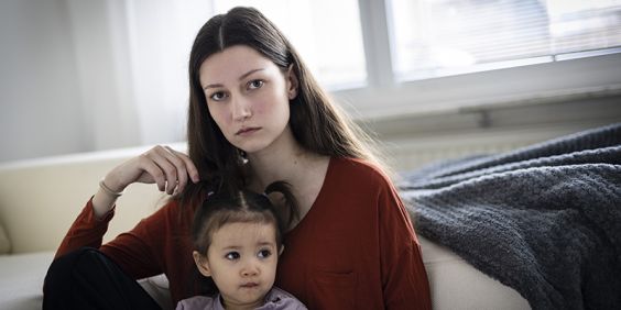 Mamma sitter med dotter i famnen och tittar in i kameran