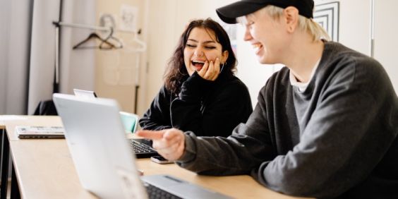 Elever på Stadsmissionens Folkhögskola pratar framför en dator.