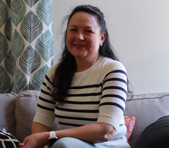 En kvinna sitter i en soffa och tittar in i kameran