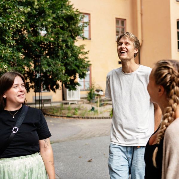 Tre människor står och pratar på en gård utanför en skola.
