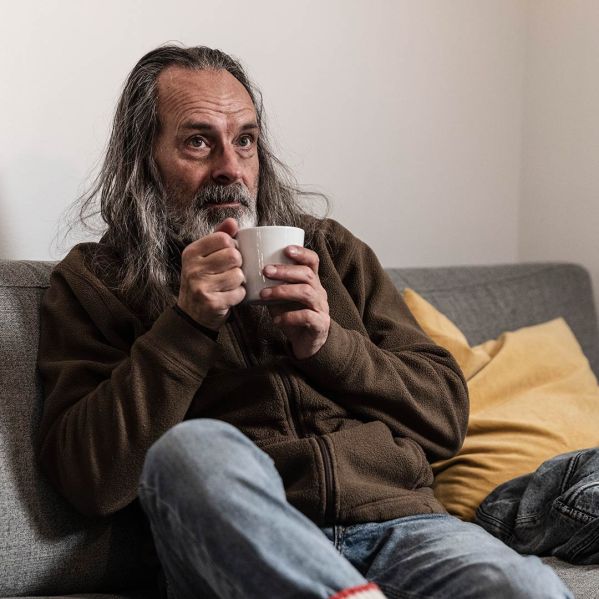 Man sitter i en soffa med en kopp kaffe i händerna.