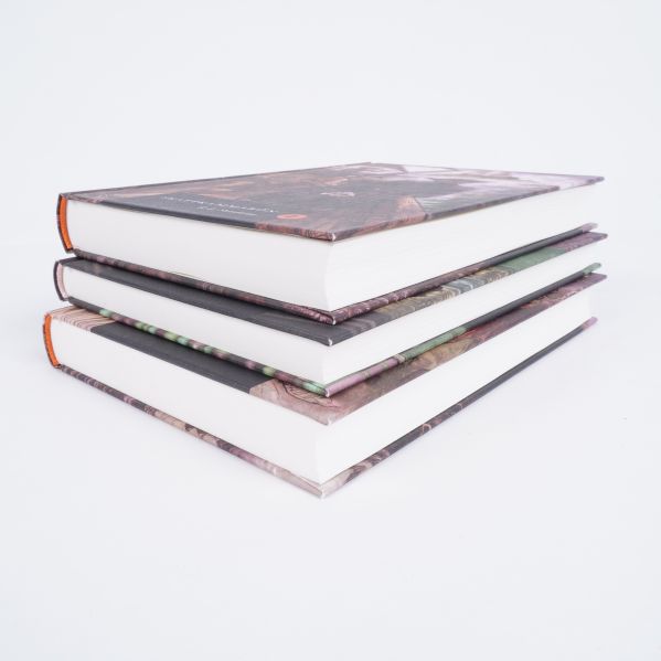 Tre inbundna böcker liggande i en hög med tjocka vita sidor