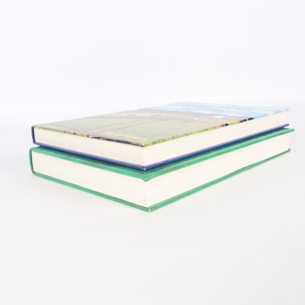 Två tjocka inbundna böcker lagda på varandra, sedd från sidan