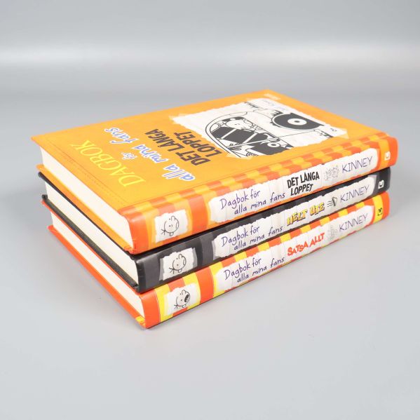 Tre böcker i stapel med hårda färgglada omslag och svarta samt orange ryggar