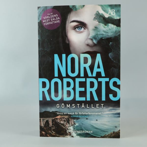 Bokomslag med titeln Gömstället av Nora Roberts, ansikte och kustmotiv