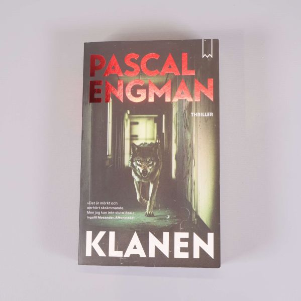 Framsida av Klanen av Pascal Engman med röd text och varg i korridor