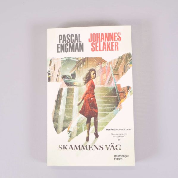 Framsida av Skammens väg med en kvinna i röd klänning på trappa