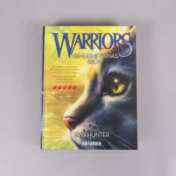 Framsidan av boken Warriors Hemligheternas skog med en katt och färgglad bakgrund