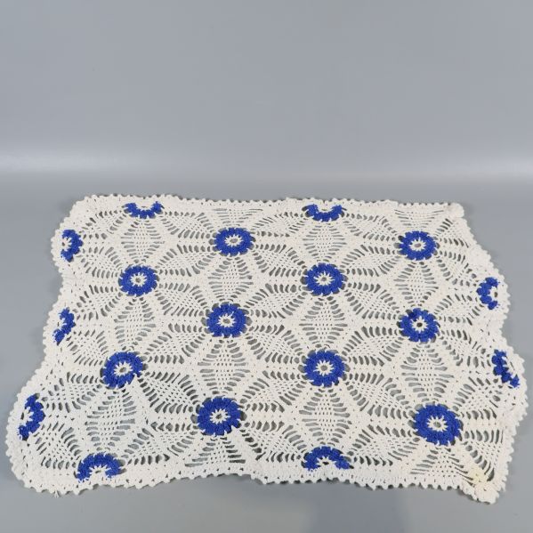 Virkad duk med blå blommor och mönster på vit botten