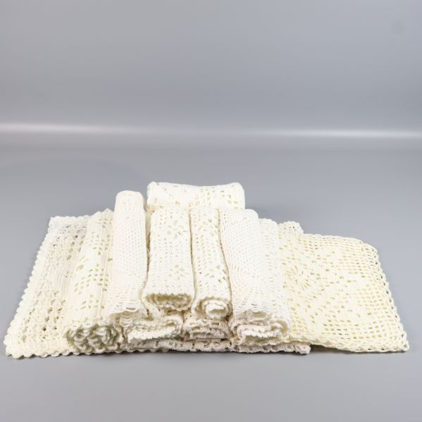 Flera hoprullade och vikta virkade dukar i krämvit färg