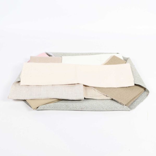 Flera tygbitar i beige och grå toner liggande på hög