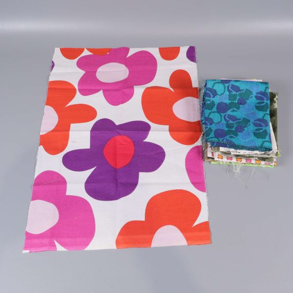 Stor tygbit med lila, röda blommor bredvid staplade tygbitar