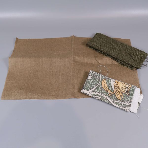 Två naturfärgade tygbitar med grov struktur och ett mönstrat stycke
