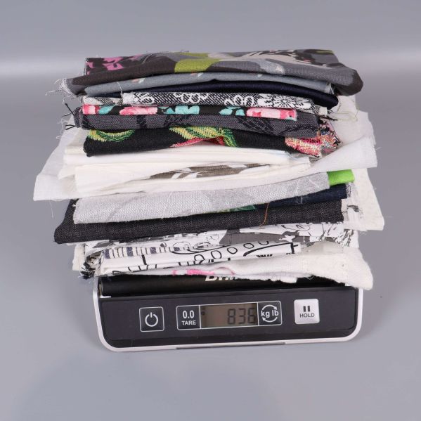 Stapel av tygbitar vägs och visar vikten 836 gram