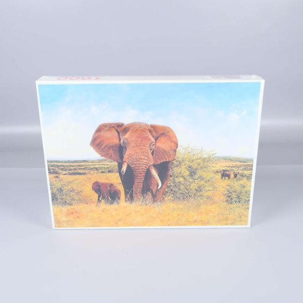 Framsidan av pussellådan visar elefanter på savannen under blå himmel