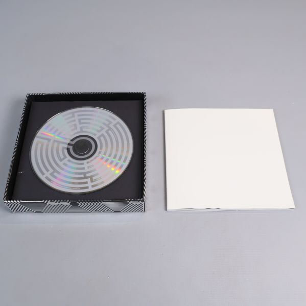 Öppen box med cd-skiva och vit bok bredvid