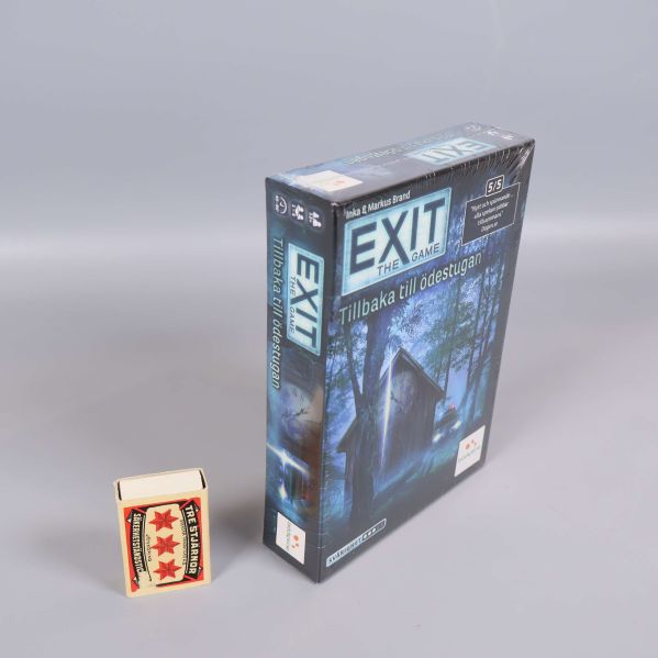 Exit the Game Tillbaka till ödestugan box stående jämte tändsticksask