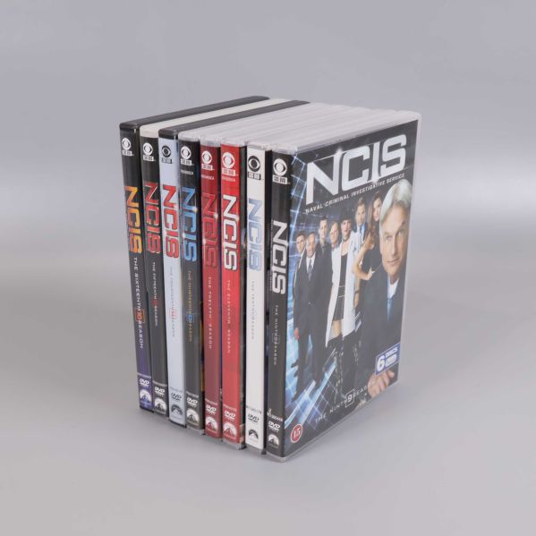 Sju NCIS DVD-boxar stående på rad med fronten synlig