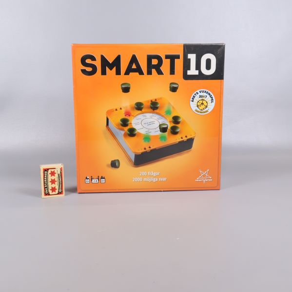 Smart 10 frågespel i orange box bredvid tändsticksask för storleksjämförelse