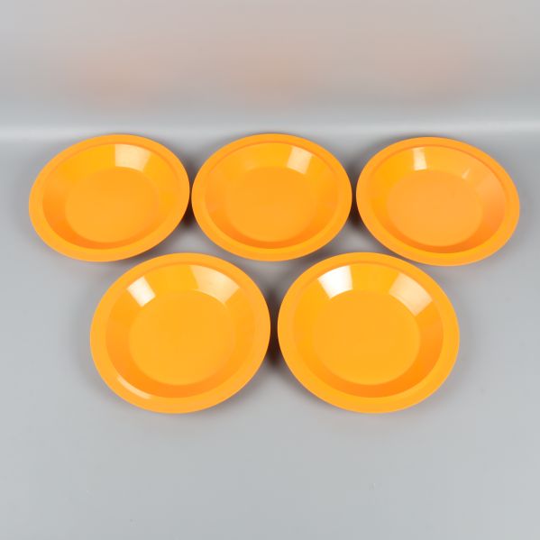 Fem orange djupa tallrikar ligger utspridda