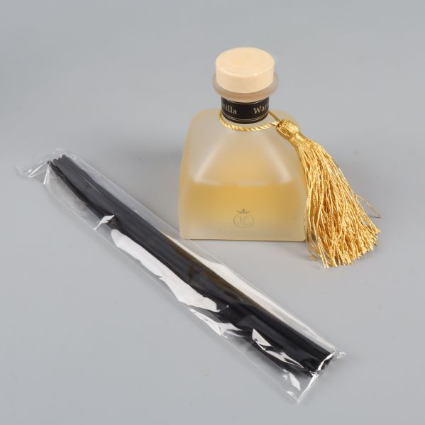 Närbild på glasflaska och svarta doftpinnar i plastpåse