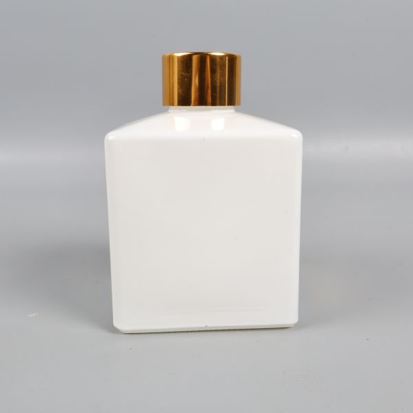 Baksidan av vit fyrkantig flaska med guldfärgat lock