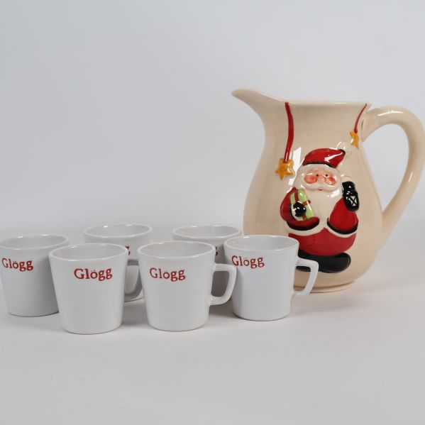 Glöggkanna med tomte och sex vita muggar framifrån